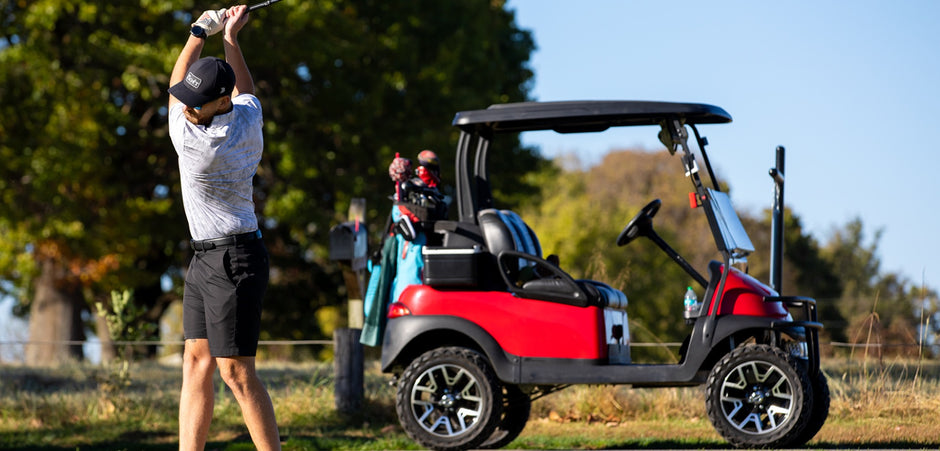 Golfer teeing off beside a red and black Pro-Guide powered golf cart
