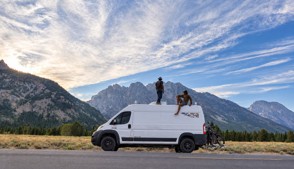 Camper van parked on a mountain road in the Tetons, two people on the roof